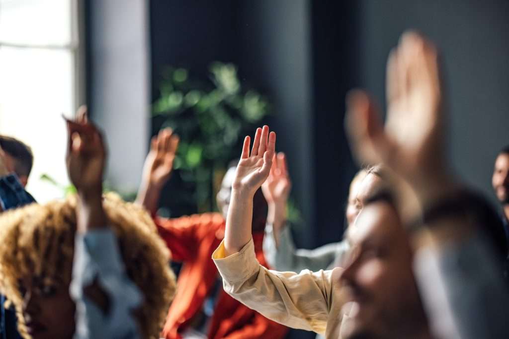 Several people from other industries raising their hands in a classroom or meeting setting.