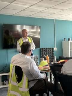 Man in safety vest presents on rigid plastics recycling to colleagues in a meeting room.