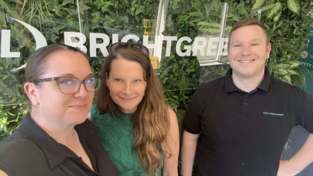 Three people smiling in front of a green wall with "IPL Brightgreen" partially visible.