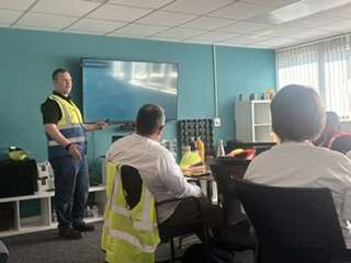 Man in a safety vest presents on rigid plastics recycling to a group in an office meeting room.